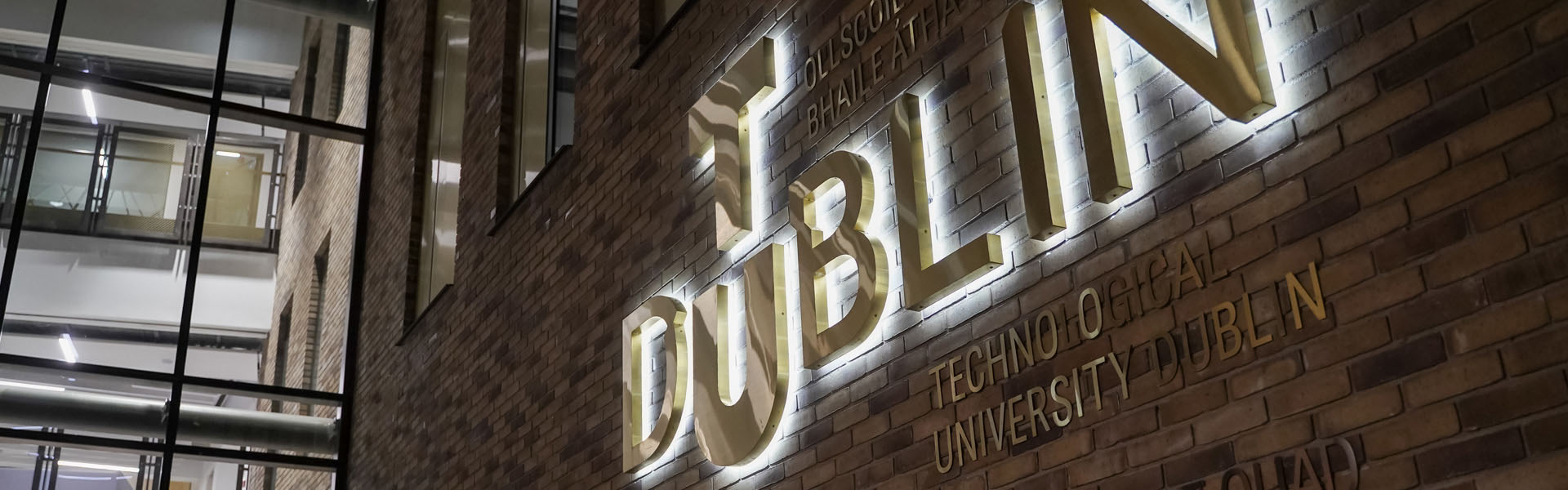 Backlit brass TU Dublin logo sign on the front entrance of the East Quad